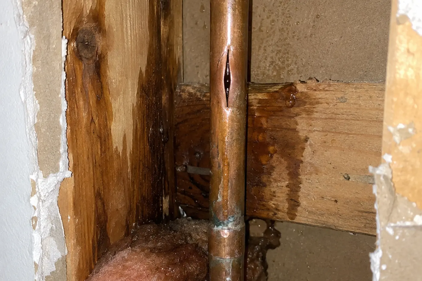 Split supply pipe inside an opened wall cavity with water running down the stud