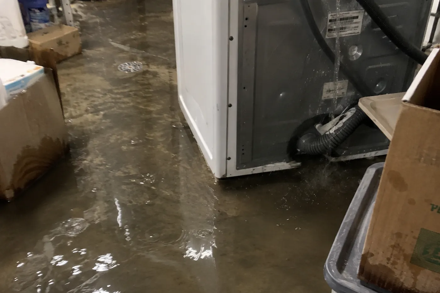 Water running from a washing machine connection across a flooded laundry room floor
