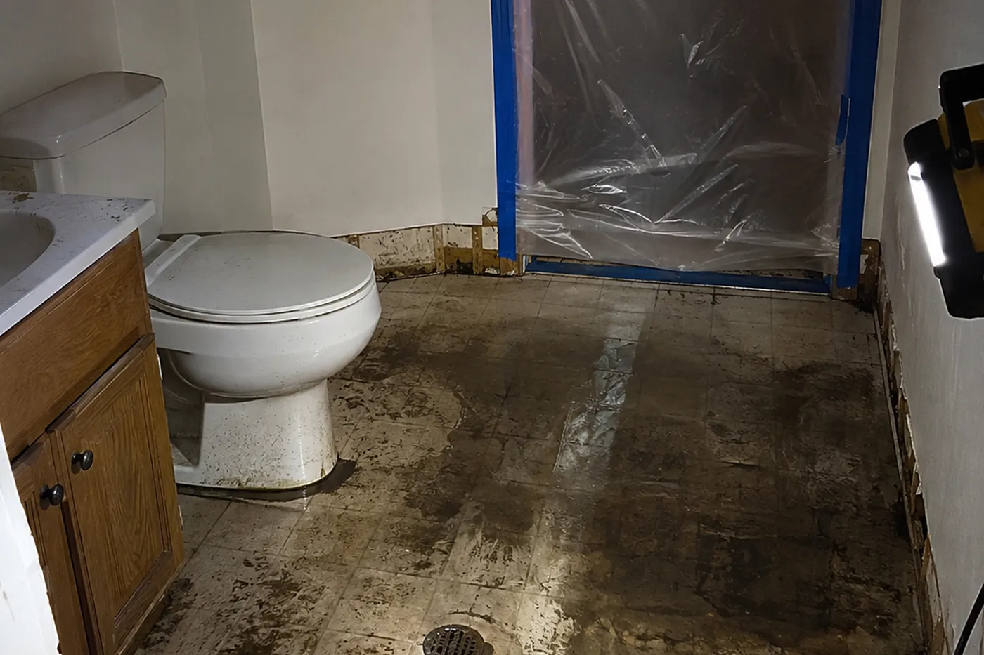 Contaminated water staining across a bathroom floor with baseboards removed and containment sheeting taped over the doorway